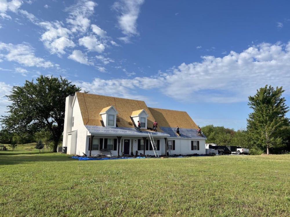 Crew replacing the roof on a two-story white farmhouse near Tulsa, fresh decking down